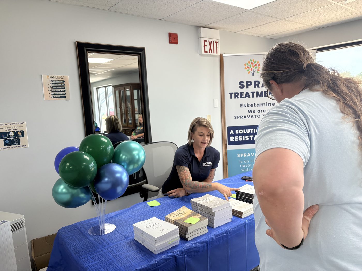 Book table with stacks of Jessica's titles, blue and teal balloons, and a visitor browsing