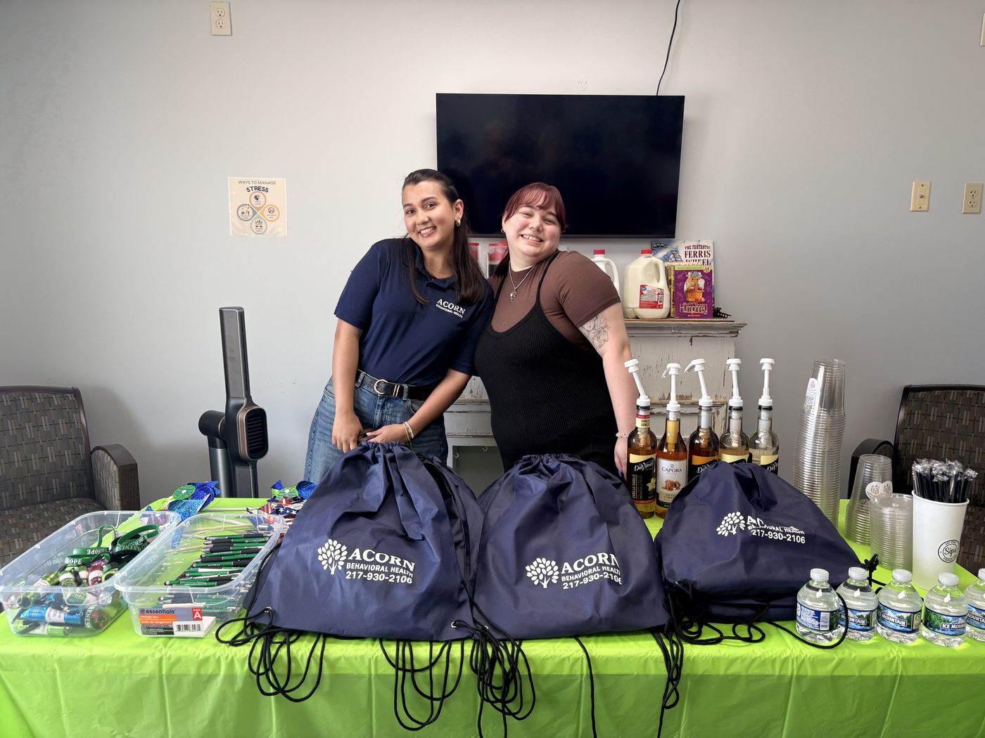 Two Acorn Behavioral Health team members smiling behind the Sips coffee station and Acorn gift bags