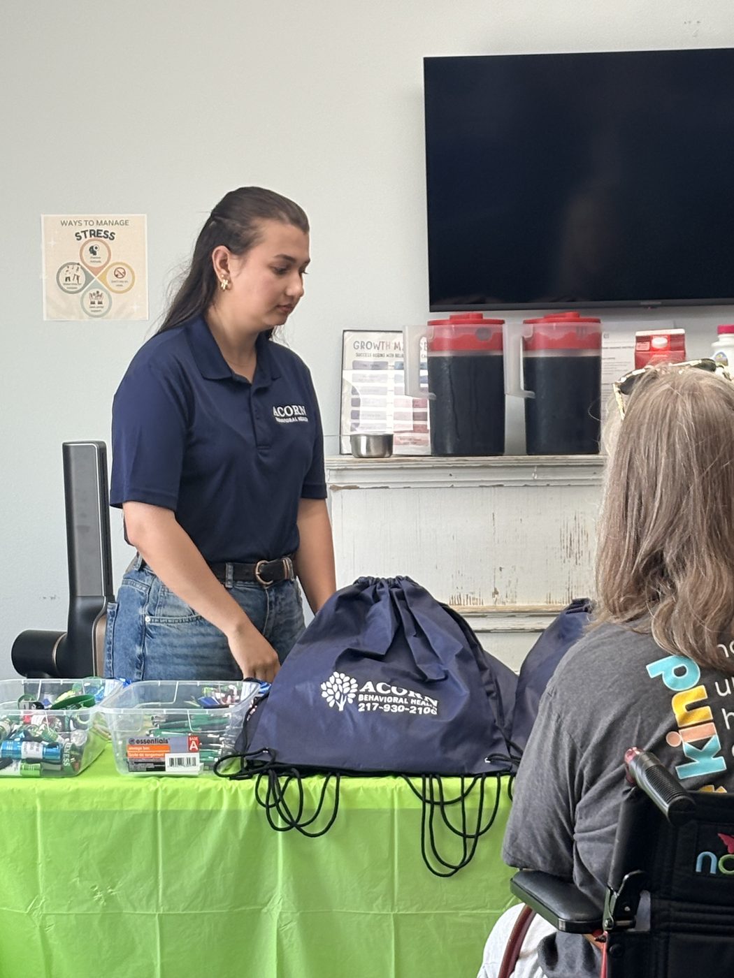 An Acorn Behavioral Health staff member handing an Acorn drawstring bag to a visitor using a wheelchair